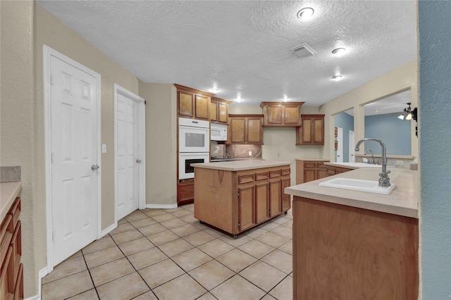 kitchen featuring ceiling fan, white appliances, light tile patterned flooring, a textured ceiling, and a kitchen island