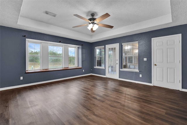 unfurnished room with ceiling fan, dark hardwood / wood-style flooring, a tray ceiling, and a textured ceiling