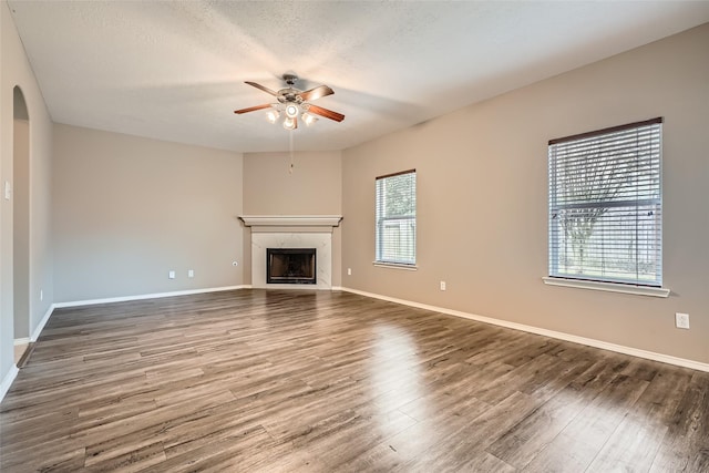 unfurnished living room with ceiling fan, a premium fireplace, a textured ceiling, and dark wood-type flooring