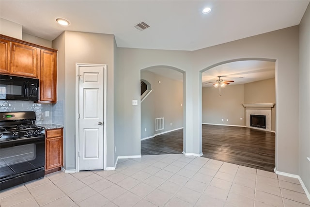 kitchen featuring light stone countertops, light tile patterned floors, black appliances, backsplash, and ceiling fan