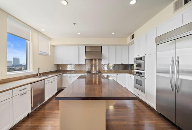 kitchen with appliances with stainless steel finishes, a center island, wall chimney range hood, and white cabinets