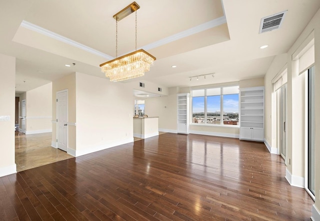 unfurnished living room featuring crown molding, dark wood-type flooring, a notable chandelier, track lighting, and a raised ceiling