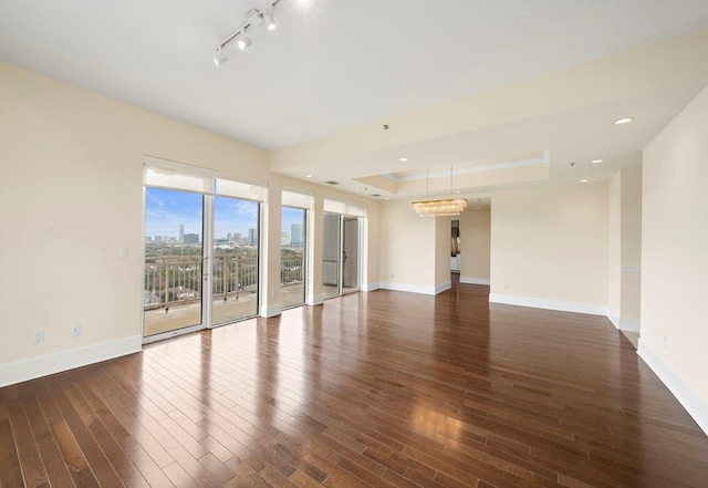 empty room featuring a raised ceiling, dark wood-type flooring, and track lighting