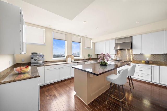 kitchen featuring a kitchen island, white cabinetry, a breakfast bar area, dark stone countertops, and wall chimney exhaust hood