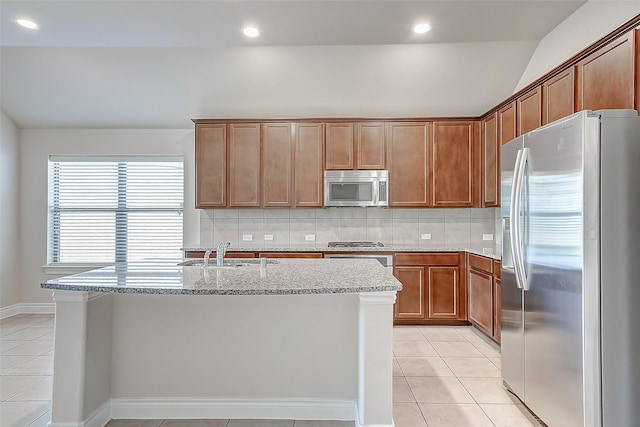 kitchen with light stone countertops, stainless steel appliances, a center island with sink, light tile patterned flooring, and sink