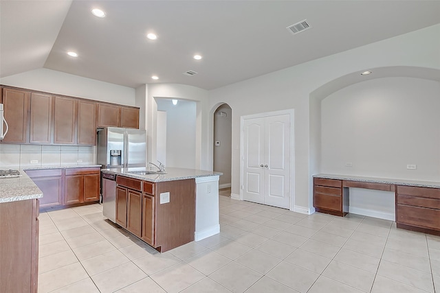 kitchen with a center island with sink, stainless steel appliances, light stone countertops, light tile patterned floors, and sink