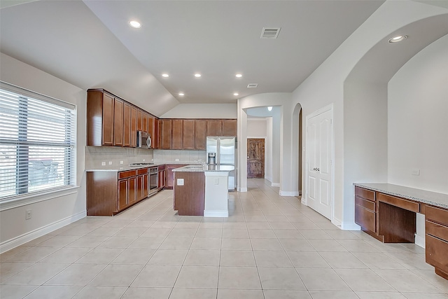 kitchen with vaulted ceiling, appliances with stainless steel finishes, light tile patterned floors, a kitchen island, and tasteful backsplash