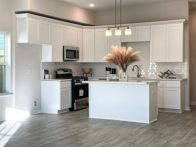 kitchen featuring stainless steel appliances, white cabinetry, sink, and hanging light fixtures