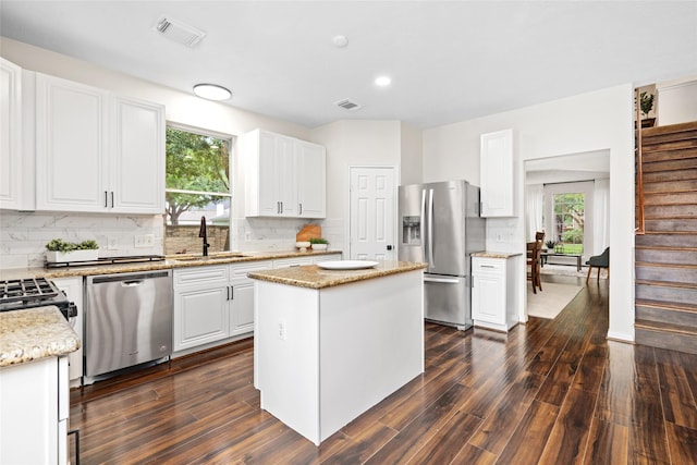 kitchen with stainless steel appliances, sink, white cabinets, a center island, and decorative backsplash