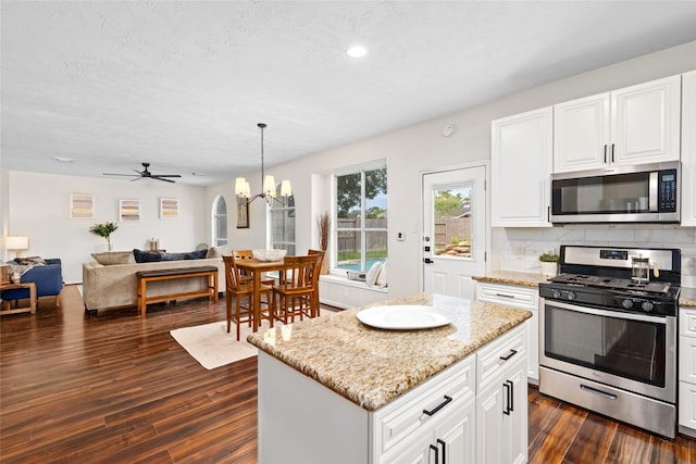 kitchen with a center island, decorative light fixtures, decorative backsplash, ceiling fan with notable chandelier, and appliances with stainless steel finishes