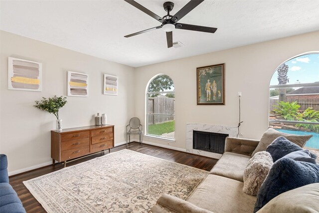 living room featuring ceiling fan, a premium fireplace, and dark hardwood / wood-style floors