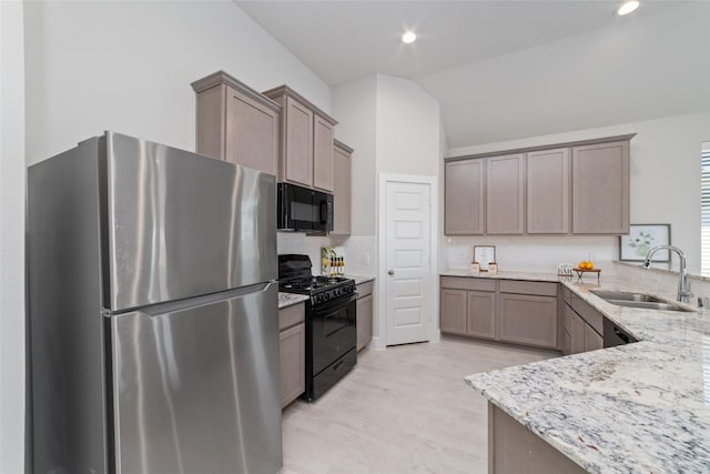 kitchen featuring vaulted ceiling, black appliances, light stone counters, sink, and tasteful backsplash