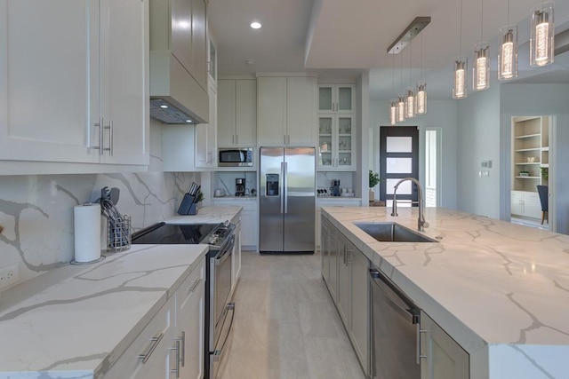 kitchen with light stone counters, pendant lighting, stainless steel appliances, an island with sink, and sink