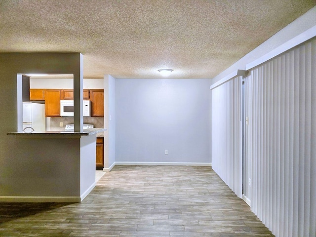 interior space featuring white appliances, light wood-type flooring, kitchen peninsula, a textured ceiling, and tasteful backsplash