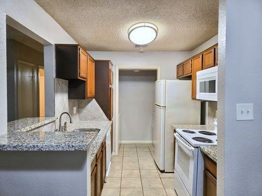 kitchen featuring white appliances, light stone counters, a textured ceiling, light tile patterned floors, and sink