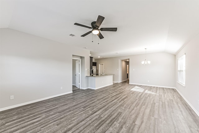 unfurnished living room with ceiling fan with notable chandelier, vaulted ceiling, and dark hardwood / wood-style floors