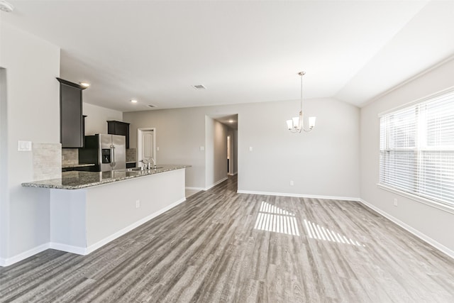 kitchen featuring light stone counters, kitchen peninsula, stainless steel fridge with ice dispenser, tasteful backsplash, and lofted ceiling