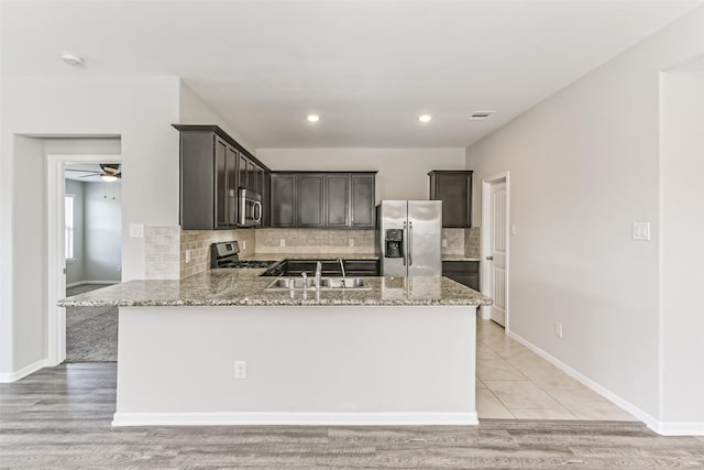 kitchen with appliances with stainless steel finishes, light stone countertops, decorative backsplash, sink, and dark brown cabinets