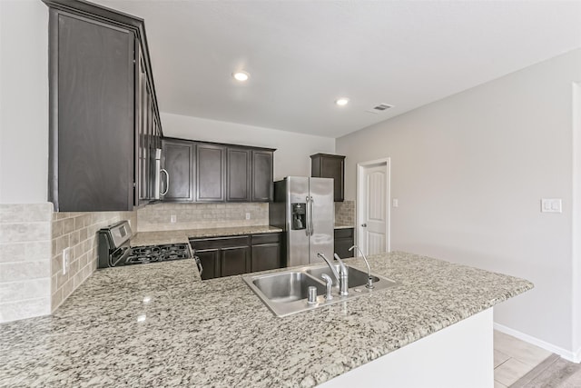 kitchen featuring light stone countertops, tasteful backsplash, appliances with stainless steel finishes, dark brown cabinets, and sink