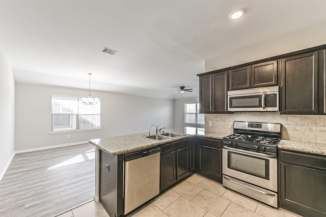 kitchen with stainless steel appliances, kitchen peninsula, pendant lighting, sink, and ceiling fan with notable chandelier