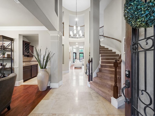 tiled foyer entrance with ornate columns, a high ceiling, a chandelier, and crown molding