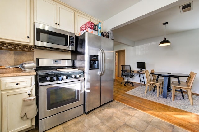 kitchen featuring cream cabinets, light hardwood / wood-style flooring, hanging light fixtures, tasteful backsplash, and appliances with stainless steel finishes