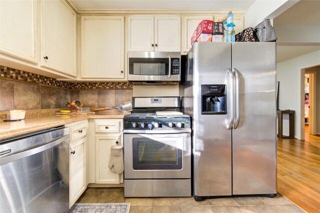 kitchen featuring stainless steel appliances, cream cabinets, tasteful backsplash, and light tile patterned floors