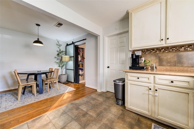 kitchen featuring decorative light fixtures, cream cabinets, backsplash, a barn door, and dark hardwood / wood-style flooring