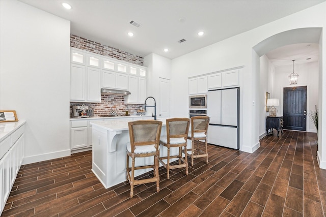 kitchen featuring hanging light fixtures, a center island with sink, a breakfast bar, black appliances, and white cabinetry