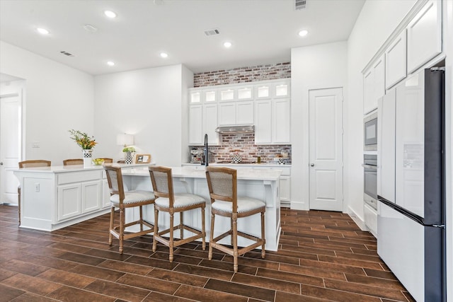 kitchen with white refrigerator, a center island with sink, white cabinets, and a breakfast bar area