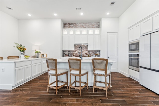 kitchen with fridge, white cabinets, stainless steel oven, a kitchen bar, and a kitchen island with sink