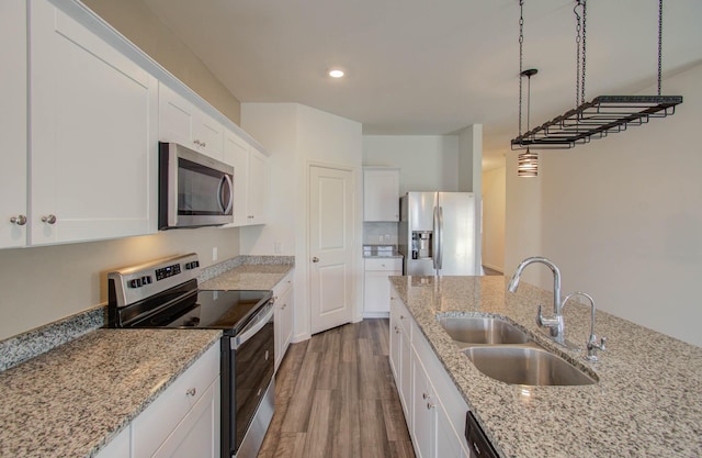 kitchen with light stone countertops, pendant lighting, white cabinetry, appliances with stainless steel finishes, and sink