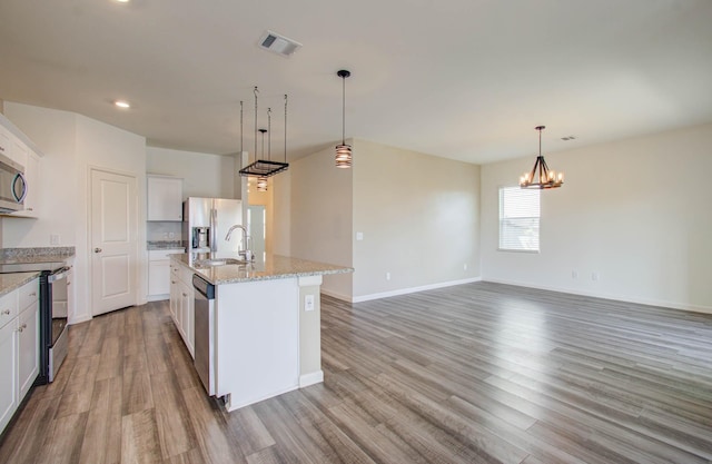 kitchen with stainless steel appliances, white cabinets, a kitchen island with sink, and a notable chandelier