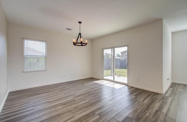 spare room featuring a notable chandelier, hardwood / wood-style floors, and a wealth of natural light