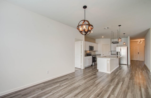 kitchen with stainless steel appliances, white cabinets, an inviting chandelier, hanging light fixtures, and a kitchen island with sink