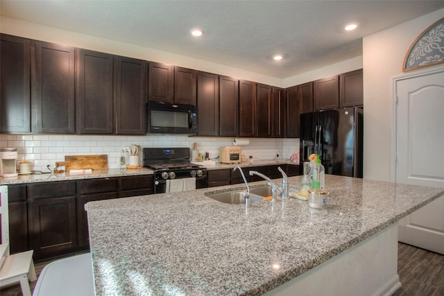 kitchen featuring light stone countertops, black appliances, and an island with sink