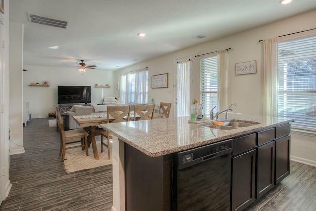 kitchen with light stone countertops, an island with sink, ceiling fan, black dishwasher, and sink