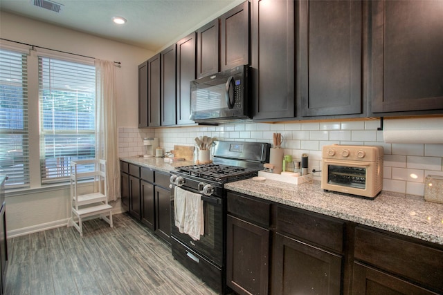 kitchen with black appliances, dark brown cabinets, light stone countertops, and hardwood / wood-style flooring