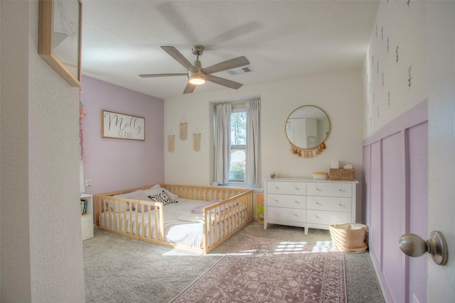 carpeted bedroom featuring ceiling fan and a crib