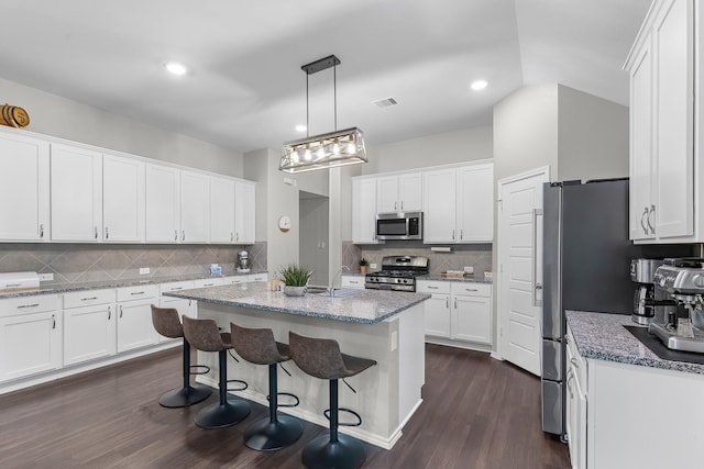 kitchen with appliances with stainless steel finishes, pendant lighting, white cabinetry, and a kitchen island