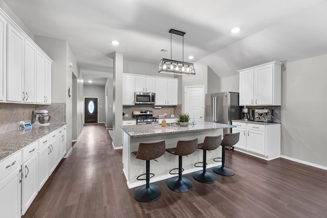 kitchen featuring vaulted ceiling, stainless steel appliances, a center island, white cabinetry, and decorative light fixtures