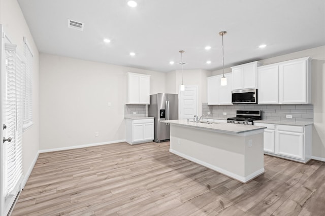 kitchen featuring stainless steel appliances, white cabinets, light hardwood / wood-style floors, hanging light fixtures, and a center island with sink