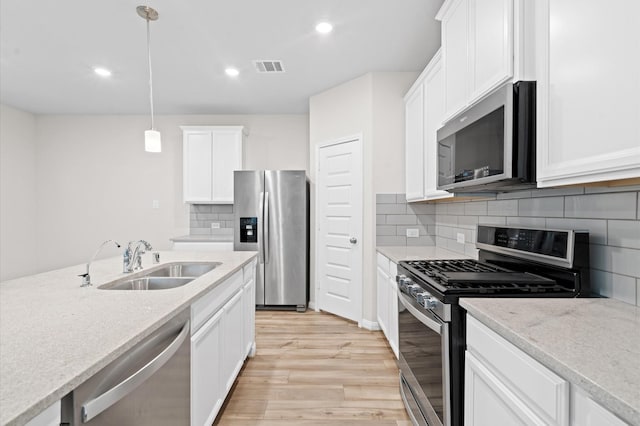 kitchen with light stone counters, hanging light fixtures, white cabinets, appliances with stainless steel finishes, and sink