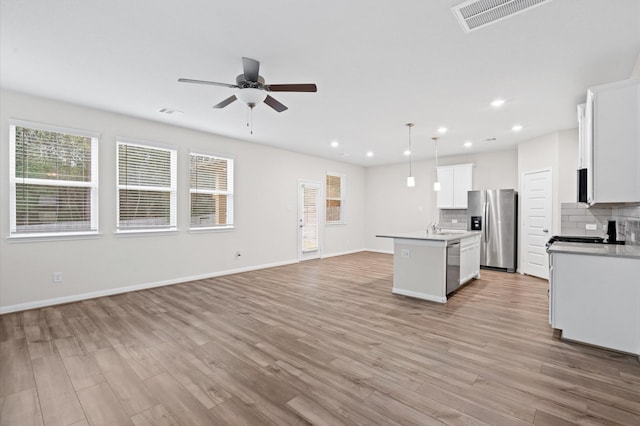 kitchen featuring stainless steel appliances, decorative light fixtures, white cabinets, decorative backsplash, and a center island with sink