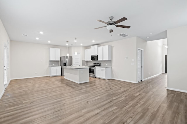 kitchen with white cabinetry, stainless steel appliances, pendant lighting, a kitchen island, and light hardwood / wood-style flooring