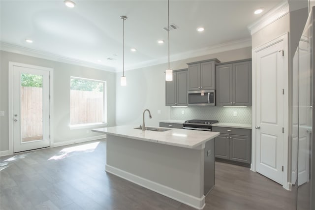 kitchen with light stone countertops, decorative light fixtures, stainless steel appliances, a kitchen island with sink, and sink