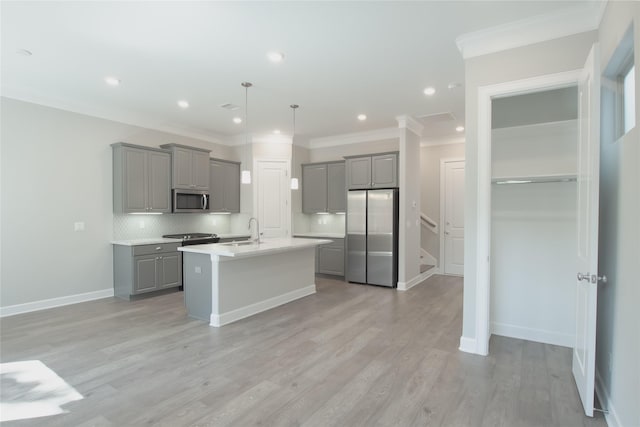 kitchen with hanging light fixtures, stainless steel appliances, an island with sink, gray cabinets, and sink