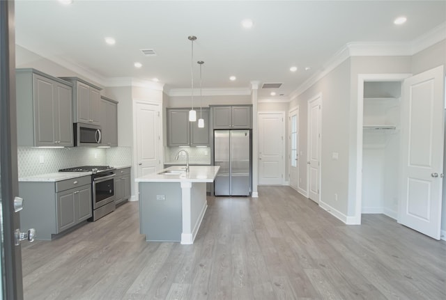 kitchen with gray cabinets, stainless steel appliances, an island with sink, pendant lighting, and sink