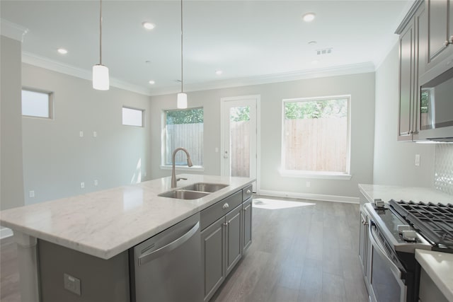 kitchen with sink, stainless steel appliances, hanging light fixtures, light stone countertops, and a center island with sink