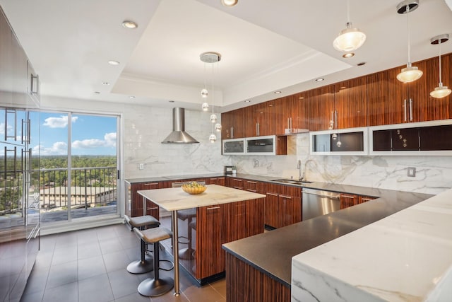 kitchen with pendant lighting, wall chimney range hood, dishwasher, and a tray ceiling